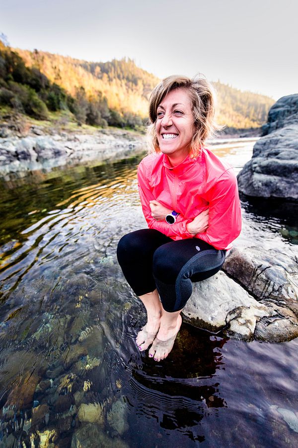 Una mujer se sienta en una roca mientras moja sus pies descalzos en un arroyo.