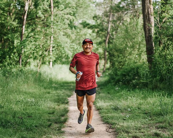 Un hombre sonríe mientras corre lentamente por el bosque.