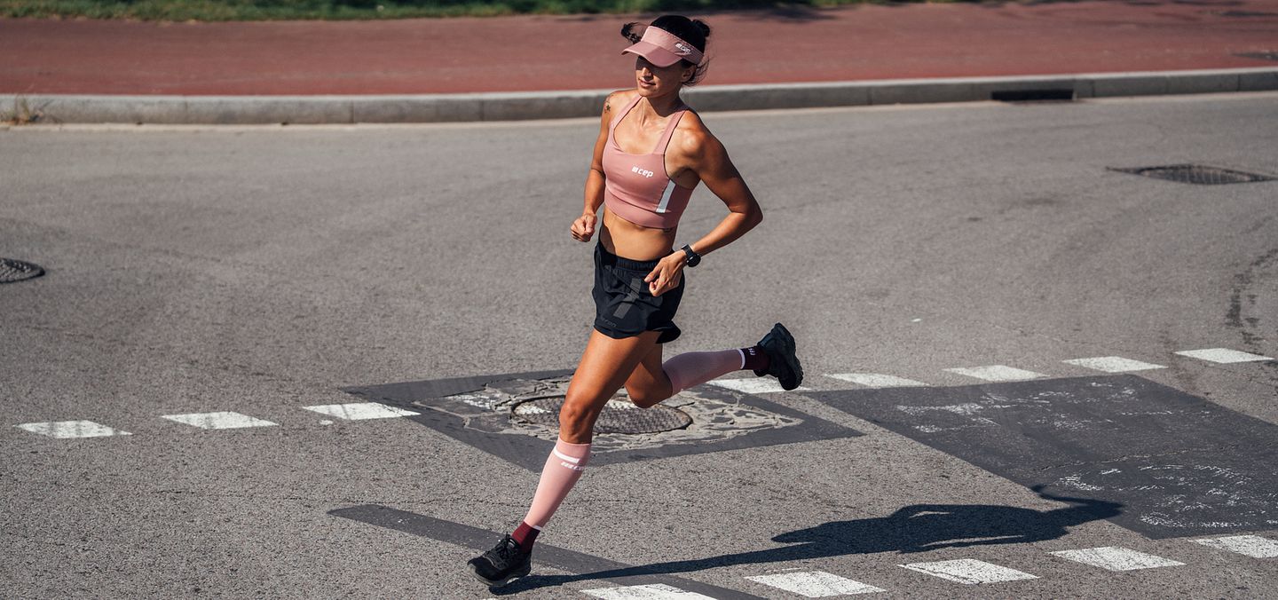 Una mujer corre con calcetines de compresión CEP 4.0 rosas
